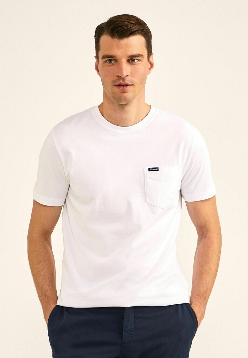 Witte katoenen t-shirt met een ronde hals, korte mouwen en een borstzak met een zwart etiket. Zachte textuur met een casual pasvorm.