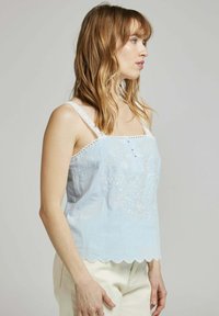 Haut sans manches bleu clair avec des motifs floraux brodés, un ourlet en forme de vagues et des bretelles en dentelle. Tissu doux avec une coupe décontractée.