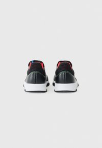 Baskets de sport noires en cuir et maille, avec une semelle blanche, des accents rouges et bleus, et des détails texturés à l'arrière.