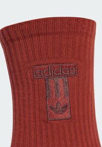 Red cotton crew sock featuring ribbed texture, an embroidered "adidas" logo, and iconic three stripes design in dark burgundy.