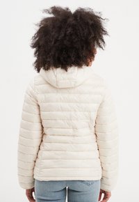 Giacca puffer beige con design a righe orizzontali, cappuccio e maniche lunghe. Texture morbida, materiale leggero e vestibilità casual ideale per essere indossata a strati.