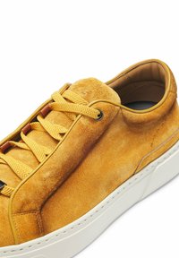 Sneaker gialla in suede con punta rotonda, suola in gomma bianca, lacci tonali e design minimalista. Presenta un rivestimento interno in pelle liscia.