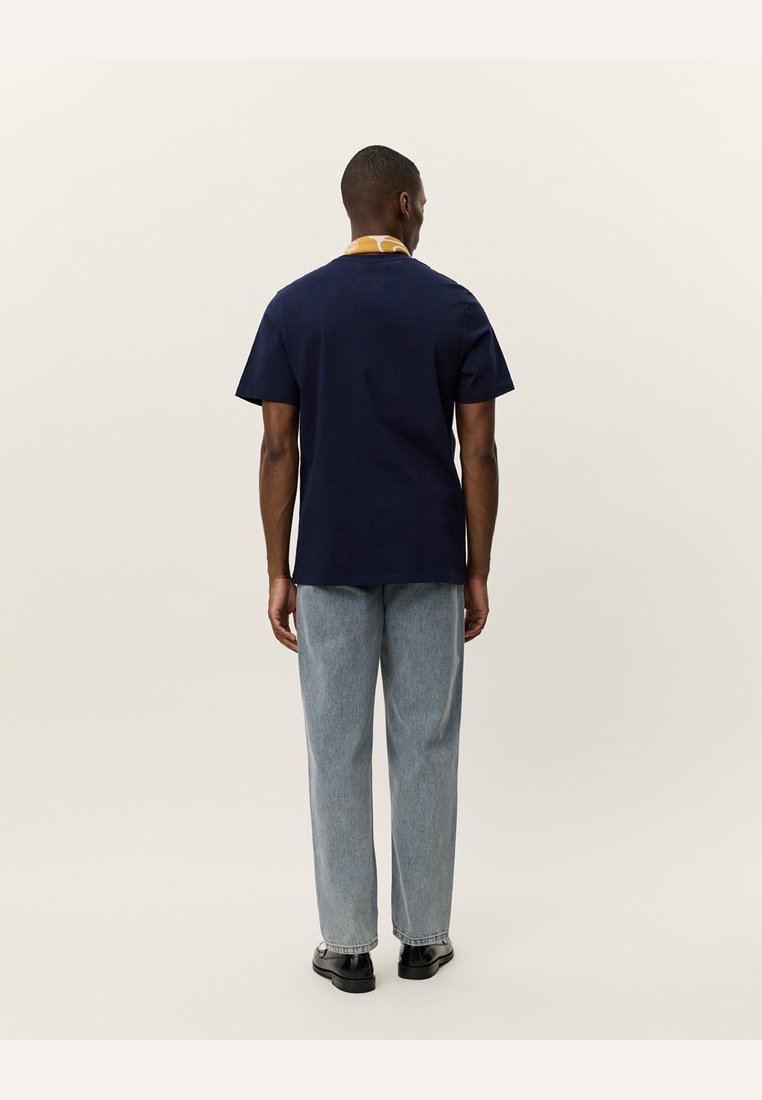Navy blue short-sleeved t-shirt with a yellow collar, paired with light blue straight-leg jeans and black shoes. Plain design, minimal detailing.