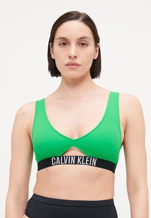Grön sportbh i ett slätt tyg. Har en djup urringning och ett svart band med "CALVIN KLEIN"-logotyp. Enkel, modern design.