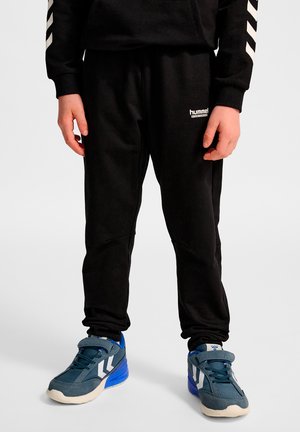 Zwarte sweatpants met een slanke pasvorm, een elastische tailleband en kniepaneelaccenten. Gecombineerd met blauwe sportschoenen met dubbele witte strepen.