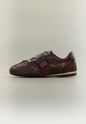 Chaussure casual en cuir marron foncé avec bride à boucle, lacets et semelle blanche, vue de côté sur fond neutre.