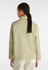 Chaqueta de estilo utilitario en verde claro, con un ajuste holgado, que presenta detalles en el cuello y las costuras de los hombros, fabricada con una tela texturada y ligera.