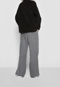 Camicia oversize in corduroy nero abbinata a jeans larghi grigi, con orlo grezzo e dettagli sulle cuciture laterali, su sfondo bianco.