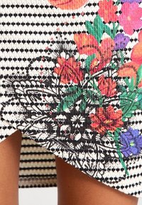 Textil a rayas en blanco y negro que presenta vibrantes patrones florales en rojo, naranja, rosa, púrpura y verde; superficie texturizada con un dobladillo asimétrico.