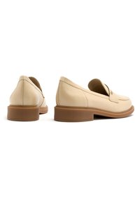 Mocassini in pelle beige con punta arrotondata, tacco basso e design slip-on. Parte superiore testurizzata con una finitura liscia e suola marrone chiaro.