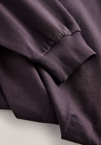 Lilla sweatshirt med lange ærmer, der har ribbede manchetter og et blødt, tekstureret stof. Minimalistisk design uden synlige logoer eller mønstre.