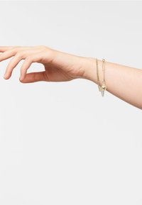Bracelet doré avec un design en maillons de chaîne, présentant un accent de boule lisse et une perle transparente. Fini brillant, léger et forme flexible.
