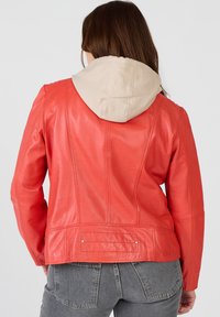 Röd läderjacka med en beige huvtröja, med en slät textur, en figursydd design och synliga sömmar på baksidan.