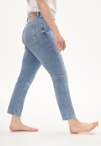 Světlé modré džíny z denimu s úzkým střihem, pěti kapsami a neupraveným lemem. Tkanina má jemnou texturu a střední výšku pasu.