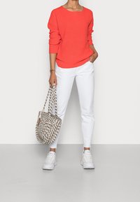 Pull rouge côtelé, pantalon blanc et sac cabas à motifs. Les baskets sont blanches avec des touches de couleur. Tenue décontractée et créative avec une coupe ample.