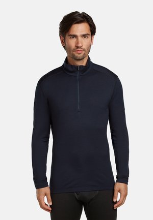 Marineblaues Zip-Hemd mit langen Ärmeln, hohem Kragen und weichem Stoff, mit dezenten Schulternähten und schlanker Passform.