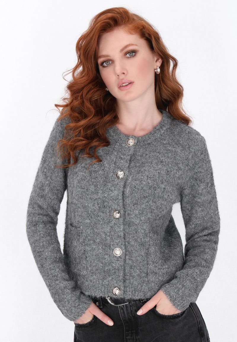Cardigan din lână gri, cu închidere frontală cu nasturi, manșete cu model în relief și două buzunare frontale. Textură moale, cu un decolteu rotund clasic.