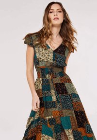 Robe à motifs multiples avec un mélange de tissus verts, bleus, orange et noirs ; manches courtes, décolleté en V et taille cintrée avec un nœud.