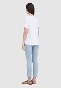 T-shirt en coton blanc, manches courtes, coupe décontractée. Associé à un jean bleu clair, avec des ourlets effilochés, une coupe slim et des sandales beiges.