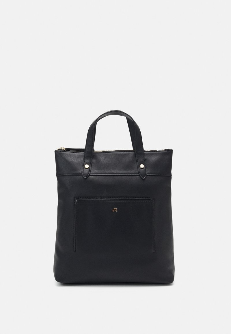 Sac cabas en cuir noir avec deux anses, une poche avant et une fermeture éclair sur le dessus, sur un fond clair uni.