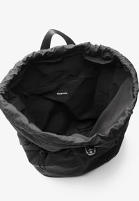 Svart tygbucketsäck med dragskoöppning, slät textur och ett innerfack med dragkedja. Har en "YOURTURN"-etikett.