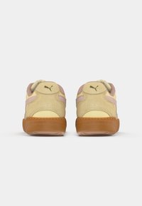 Ett par beige och rosa mockaskor med gummisulor, sedda bakifrån, med en svart Puma-logotyp på varje hälflik.