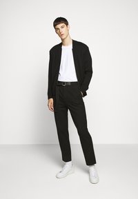 Black bomber jacket over a white t-shirt, paired with tailored black pants and white sneakers. Slim fit, smooth fabric, minimalistic design.