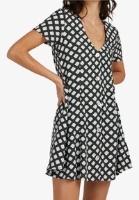 Robe noire à motif floral blanc, manches courtes, encolure en V et boutons à l'avant ; en tissu léger avec une jupe évasée.