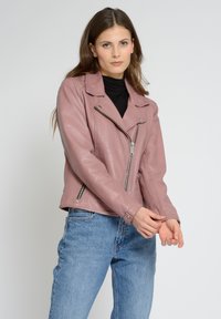 Veste de moto en cuir rose avec un col à revers, fermeture éclair asymétrique et poches latérales zippées. Portée sur un haut noir et associée à un jean bleu.