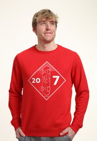 Felpa rossa con maniche lunghe, caratterizzata da un motivo grafico bianco di uno skateboard e dai numeri "20" e "7" all'interno di una forma a diamante.