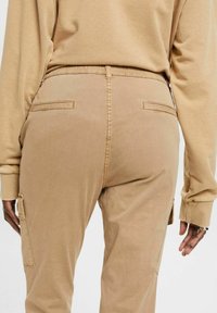 Beige cargobyxor med en texturerad yta, med dragsko i midjan, två bakfickor och sidofickor för cargo.