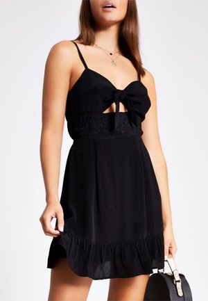 Sort kjole med sløjfe foran, udskårne detaljer, broderet taljebånd og flæsekant. Fremstillet af letvægtsstof. Glat tekstur.