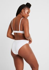 Vitt bomullsbehå och set med högmidjade trosor, med justerbara axelband och en sömlös design för komfort. Slät textur och minimalistisk stil.