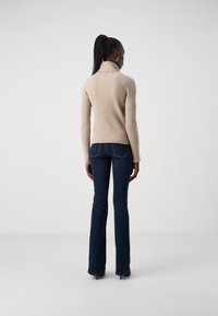 Pull à col roulé beige côtelé avec une silhouette ajustée et un col rabattu, associé à un jean évasé bleu foncé et des escarpins noirs.
