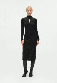 Vestido preto de manga longa com decote em forma de olho de fechadura, silhueta elegante, textura canelada e comprimento médio. Usado com botas de salto alto até o joelho.