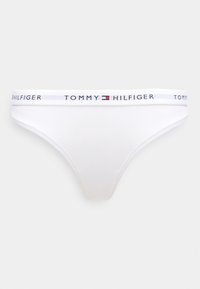 Biele bavlnené tangá s pružným pásom, na ktorom je nápis "TOMMY HILFIGER" v čiernej, červenej a modrej farbe. Jednoduchý dizajn a hladká textúra.