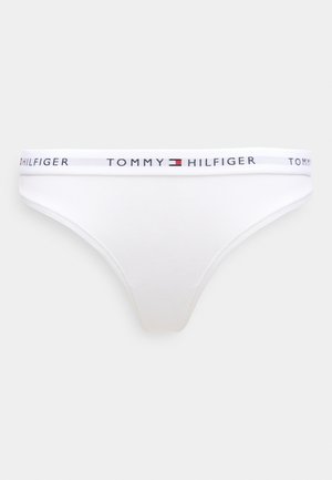 Valkoinen puuvillainen stringit-pikkuhousu, jossa joustava vyötärönauha ja "TOMMY HILFIGER" -logo mustalla, punaisella ja sinisellä tekstillä. Yksinkertainen muotoilu ja sileä pinta.