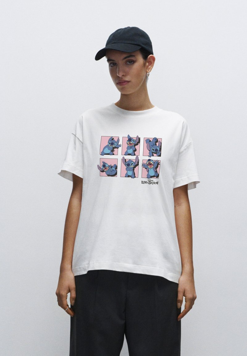 Hvid bomulds T-shirt med et farverigt grafisk motiv af en tegneseriefigur i seks positioner på en lyserød baggrund. Korte ærmer og afslappet pasform.