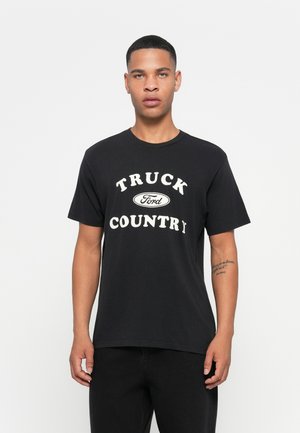 Zwarte katoenen t-shirt met opvallende witte tekst "TRUCK Ford COUNTRY." Korte mouwen, ronde hals en een relaxte pasvorm. Eenvoudig ontwerp.