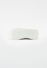 Semelle de chaussure avec une base en caoutchouc blanc, texture striée, forme arrondie, bords lisses et légère courbure ascendante au niveau de la zone des orteils.