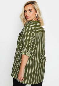 Blusa verde a righe con maniche arrotolate, colletto a bottoni e dettaglio sul retro. Il tessuto è morbido e ha una vestibilità rilassata.