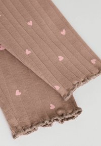 Leggings bruns à côtes ornés de petits motifs en forme de cœur roses et de bords froncés. Texture douce avec un matériau élastique pour le confort et l'ajustement.