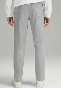 Pantaloni gri dintr-o țesătură ușoară și netedă, având un design conic, două buzunare la spate și purtați cu adidași albi.