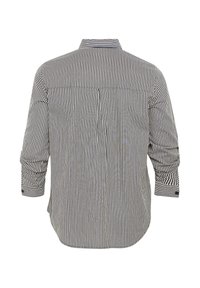 Chemise à manches longues boutonnée avec des rayures verticales étroites noires et blanches, vue de dos avec les manches légèrement retroussées.