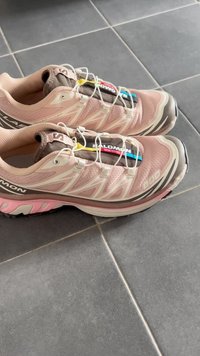 Salomon terepfutó cipők világos rózsaszín hálós felsőrésszel, barna részletekkel és gumitalppal; rugalmas fűzőkkel és párnázott nyelvvel rendelkezik.