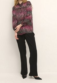 Långärmad blus i svart med rosa och vita prickar, kombinerad med svarta, skräddarsydda byxor och svarta pumps med spetsig tå.