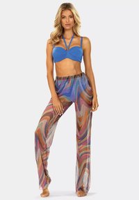 Niebieski crop top na halter z detalem w formie skrętu, w połączeniu z luźnymi, przezroczystymi spodniami w kolorowy wir w odcieniach różu, pomarańczu i purpury.