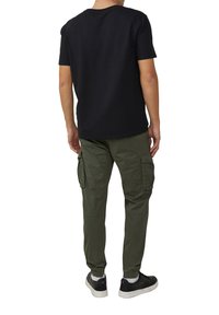 Zwarte kortekragen textuur shirt, olijfgroene cargo broek met elastische boorden en zijzakken, gedragen met zwarte sneakers.
