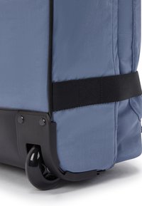 Close-up of blue fabric luggage corner with black plastic protective base and wheel, secured by a black strap.