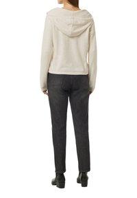 Hellbeige, verkürzter Hoodie mit Kapuze, weicher Textur, kombiniert mit dunklen, leicht strukturierten Jeans mit schmalem Bein und dezentem Nähdetails.